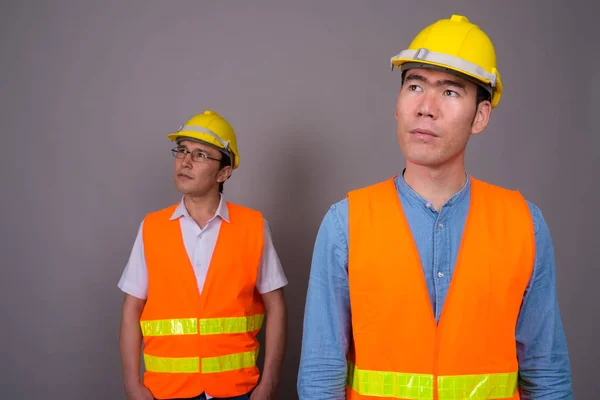 Dos jóvenes asiáticos trabajadores de la construcción juntos contra ba gris —  Fotos de Stock