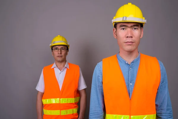 Dos jóvenes asiáticos trabajadores de la construcción juntos contra ba gris —  Fotos de Stock