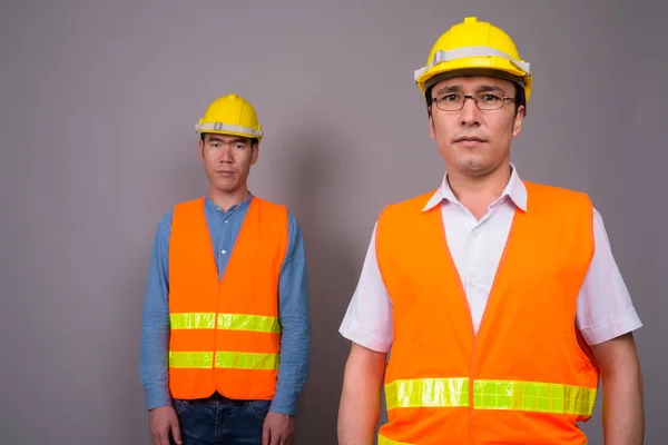 Dos jóvenes asiáticos trabajadores de la construcción juntos contra ba gris —  Fotos de Stock