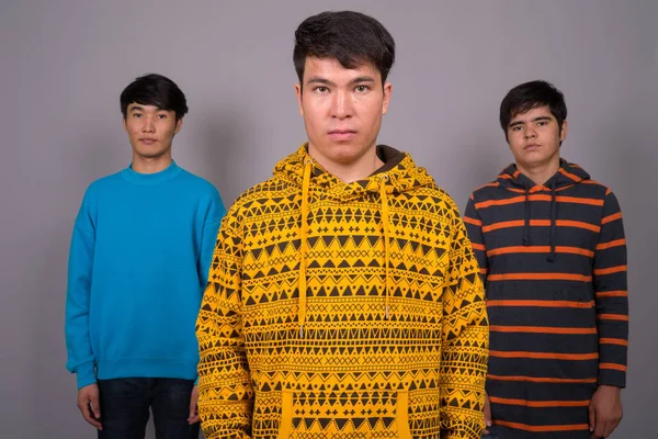 Trois jeunes amis asiatiques ensemble sur fond gris — Photo