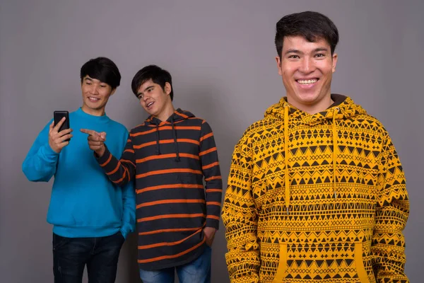 Três jovens amigos asiáticos juntos contra fundo cinza — Fotografia de Stock