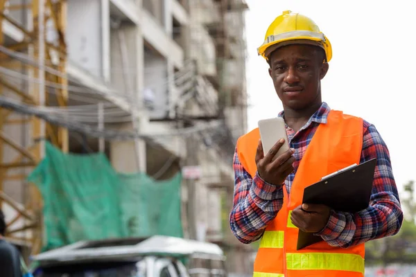 Joven negro africano hombre construcción trabajador sosteniendo portapapeles un —  Fotos de Stock