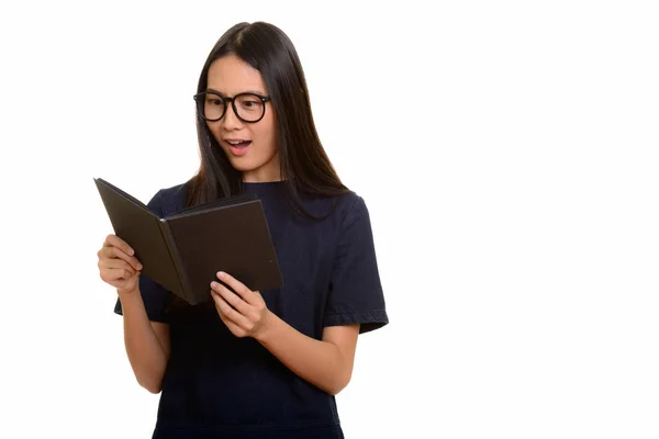Young beautiful Asian teenage girl reading book while looking sh — Stock Photo, Image