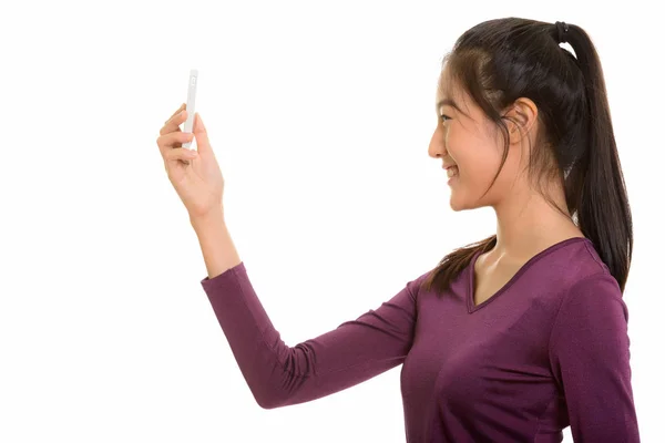 Profile view of young happy Asian teenage girl smiling while tak — Stock Photo, Image