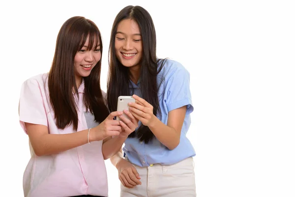 Two young happy Asian teenage girls smiling and using mobile pho — Stock Photo, Image