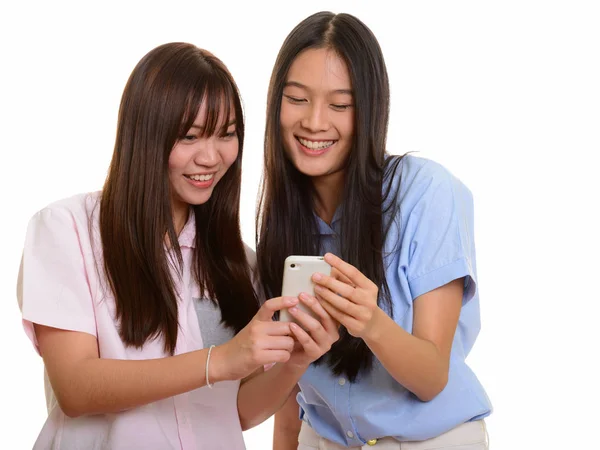 Two young happy Asian teenage girls smiling and using mobile pho — Stock Photo, Image