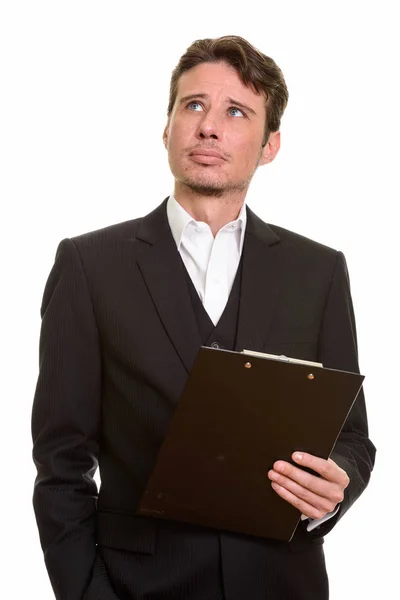 Handsome Caucasian businessman thinking while holding clipboard — Stock Photo, Image