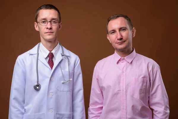 Молодой человек врач и пациент на коричневом фоне — стоковое фото
