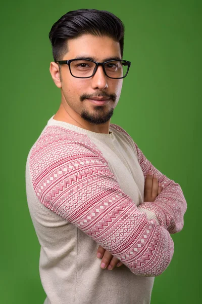 Studio shot of young bearded Iranian man wearing casual clothes against green background