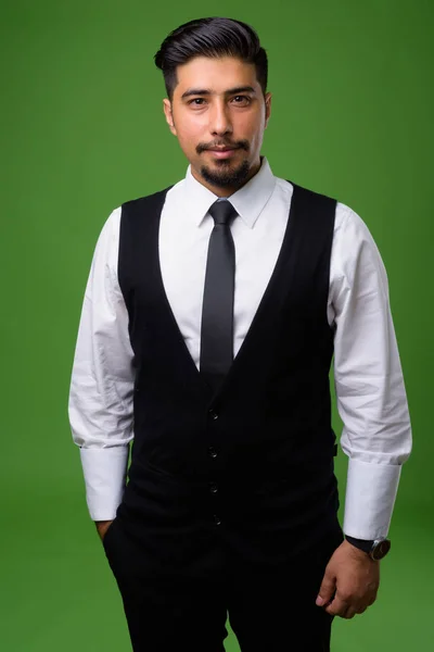 Young bearded Iranian businessman against green background