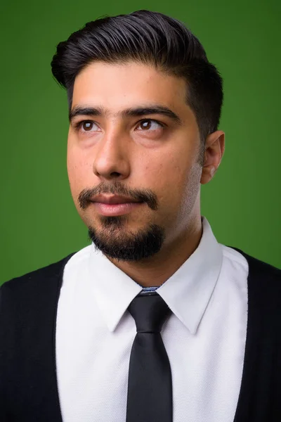 Young bearded Iranian businessman against green background