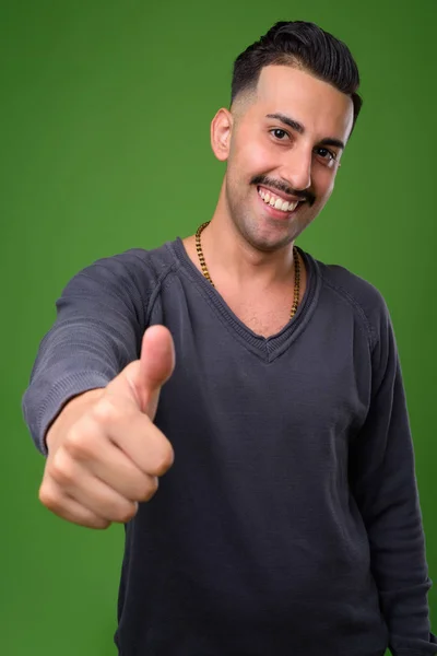 Junger schöner iranischer Mann mit Schnurrbart vor grünem Hintergrund — Stockfoto