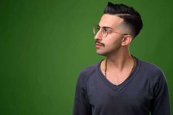 Young handsome Iranian man with mustache against green backgroun