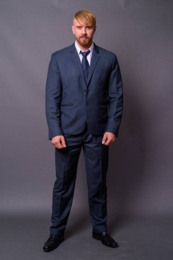 Sakallı iş adamı, sarı saçlı, gri arka planda.