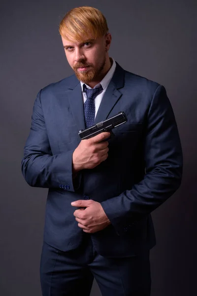 Homem de negócios barbudo com pistola contra fundo cinza — Fotografia de Stock