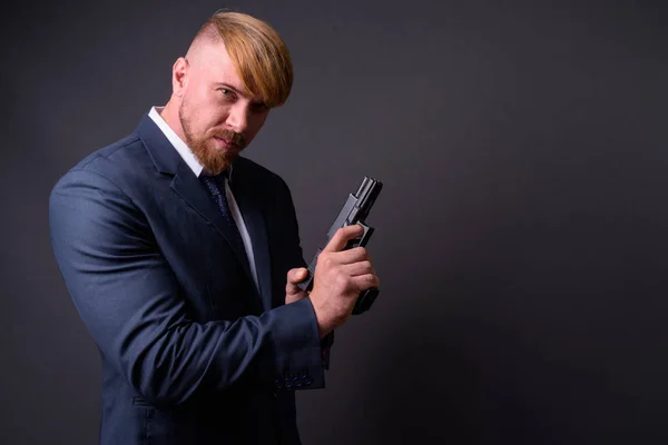 Empresario barbudo con pistola contra fondo gris —  Fotos de Stock