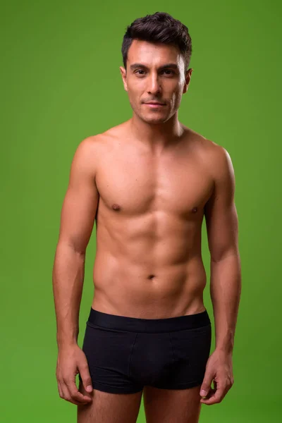 Young handsome Hispanic man shirtless against green background — Stock Photo, Image