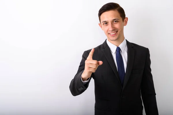 Studioaufnahme eines jungen glücklichen Geschäftsmannes, der lächelt, während er auf die Kamera zeigt — Stockfoto
