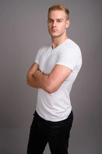Sarı saçlı, gri arka planda genç yakışıklı bir adam.