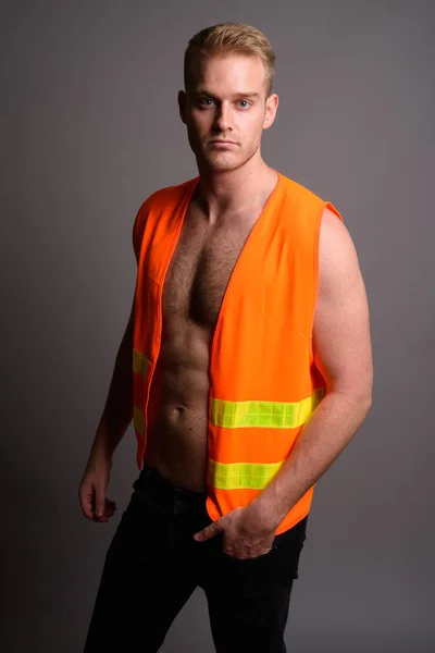 Joven hombre guapo trabajador de la construcción sin camisa contra ba gris — Foto de Stock