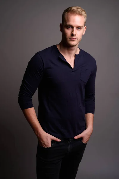 Sarı saçlı, gri arka planda genç yakışıklı bir adam.