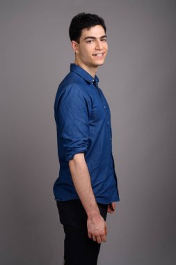 Gri arka planda mavi gömlek giyen genç ve yakışıklı işadamının stüdyo fotoğrafı.