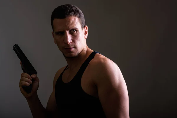 Estudio disparo de joven musculoso persa hombre sosteniendo arma mientras delgada —  Fotos de Stock