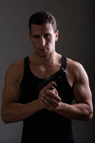 Studio shot of young muscular Persian man holding gun and lookin