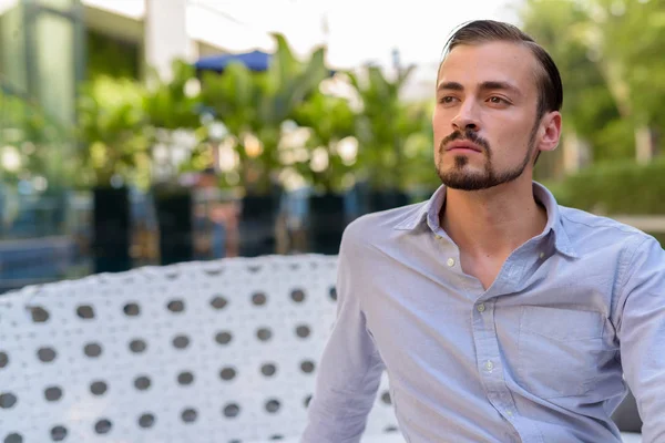 Portrait de jeune homme barbu à la mode assis à l'extérieur — Photo