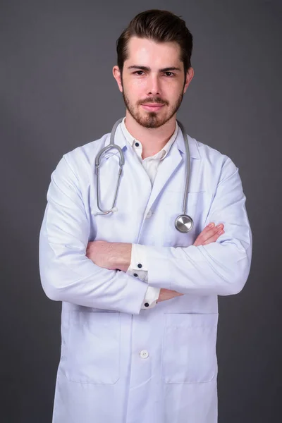 Mladý hezký vousatý muž lékař proti šedé pozadí — Stock fotografie