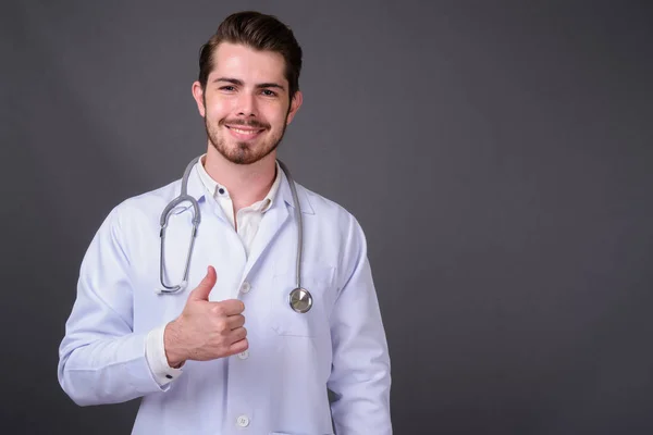 Mladý hezký vousatý muž lékař proti šedé pozadí — Stock fotografie