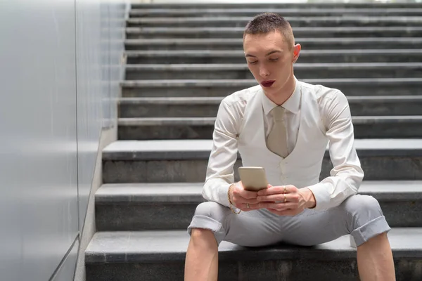 Νεαρός ανδρόγυνο ομοφυλοφιλικές επιχειρηματίας Lgtb κάθεται σε σκάλες, κατά τη χρήση του τηλεφώνου — Φωτογραφία Αρχείου