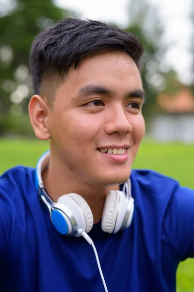 ヘッドフォンを身に着けている公園でリラックスした若いのハンサムなアジア男 — ストック写真