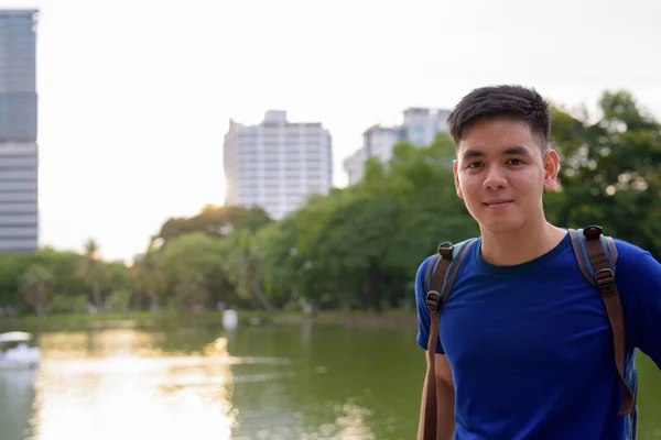 タイのバンコクの公園でリラックスしたバックパックを持つ若いハンサムなアジアの観光客の男の肖像 — ストック写真
