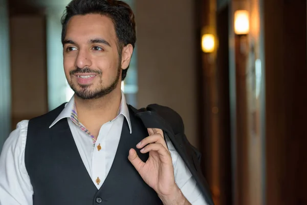 Young happy Indian man smiling while holding jacket and looking