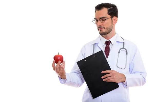 工作室拍摄的年轻帅哥医生抱着剪贴板 看着红红的苹果 — 图库照片