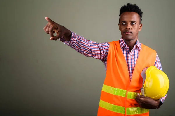 Joven hombre africano guapo trabajador de la construcción contra el color b — Foto de Stock