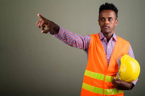 Joven hombre africano guapo trabajador de la construcción contra el color b —  Fotos de Stock