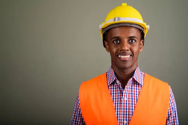 Joven hombre africano guapo trabajador de la construcción contra el color b — Foto de Stock