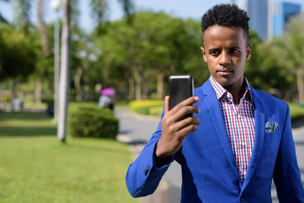 Joven empresario africano guapo usando el teléfono móvil a la par — Foto de Stock