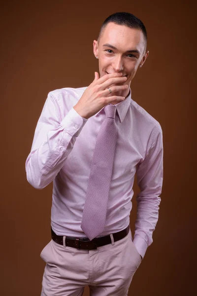 Joven hombre de negocios andrógino guapo sobre fondo marrón — Foto de Stock