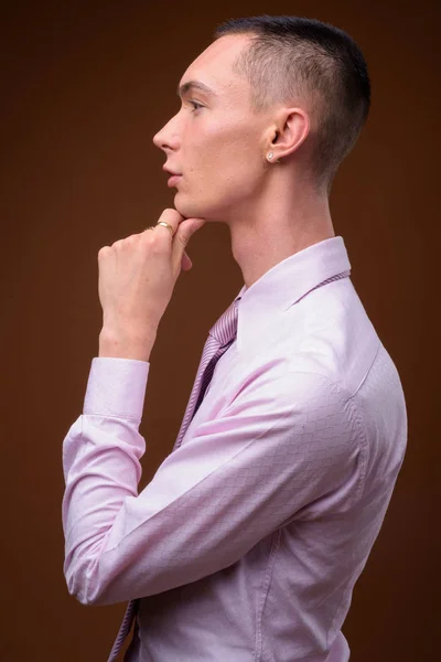 Young handsome androgynous businessman against brown background — Stock Photo, Image