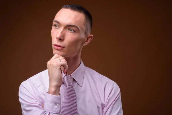 Junger hübscher androgyner Geschäftsmann mit braunem Hintergrund — Stockfoto