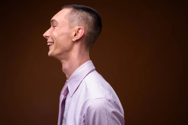 Young handsome androgynous businessman against brown background — Stock Photo, Image