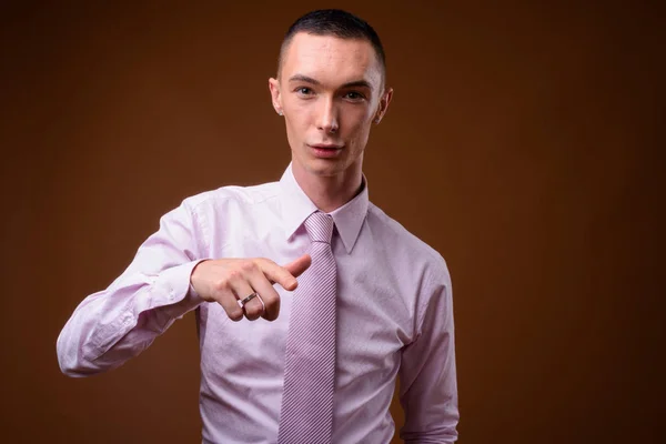 Junger hübscher androgyner Geschäftsmann mit braunem Hintergrund — Stockfoto