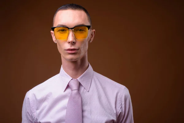 Young handsome androgynous businessman against brown background — Stock Photo, Image