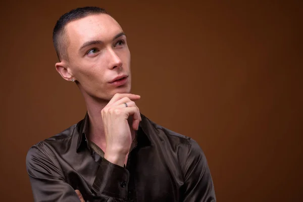 Young handsome androgynous businessman against brown background — Stock Photo, Image