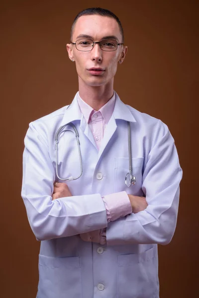 Young handsome androgynous man doctor against brown background