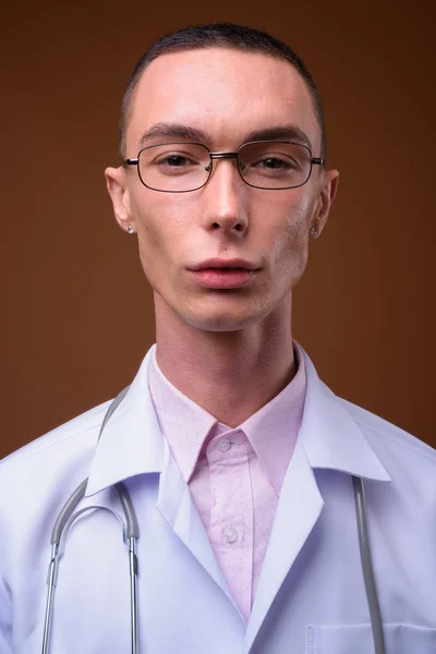 Jonge knappe man van de androgyne arts tegen bruine achtergrond — Stockfoto