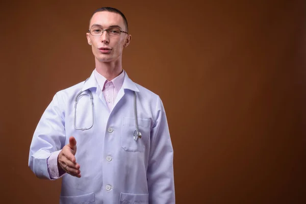 Jovem bonito homem andrógino médico contra fundo marrom — Fotografia de Stock